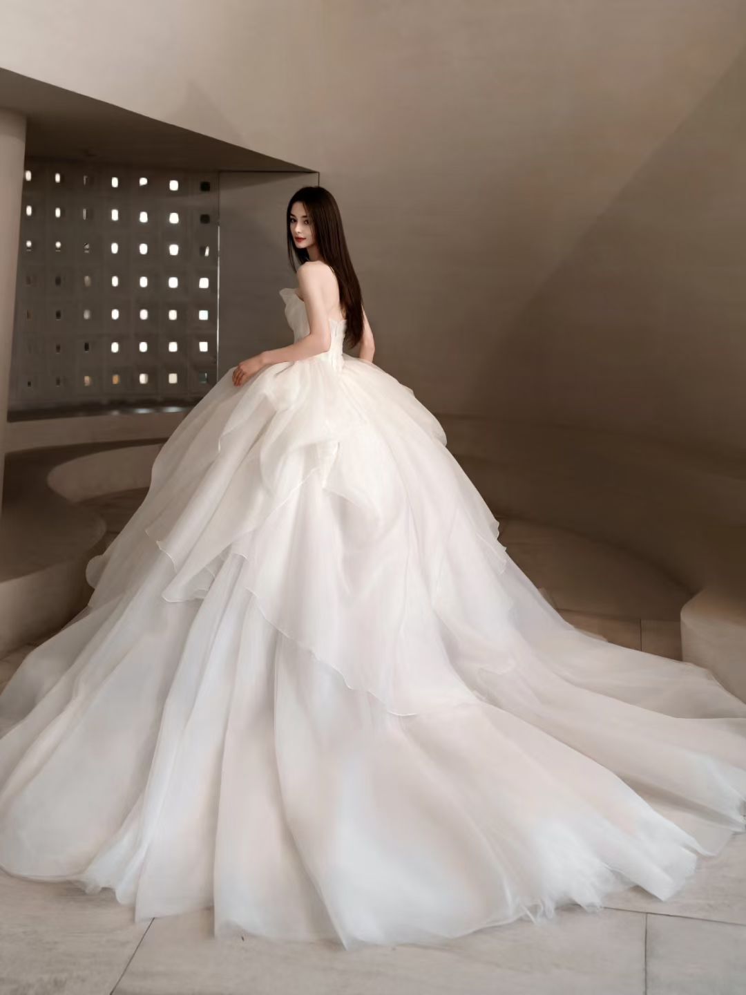Back view of Luxury strapless organza ball gown wedding dress with layered skirt, floral hip detail and dramatic long train