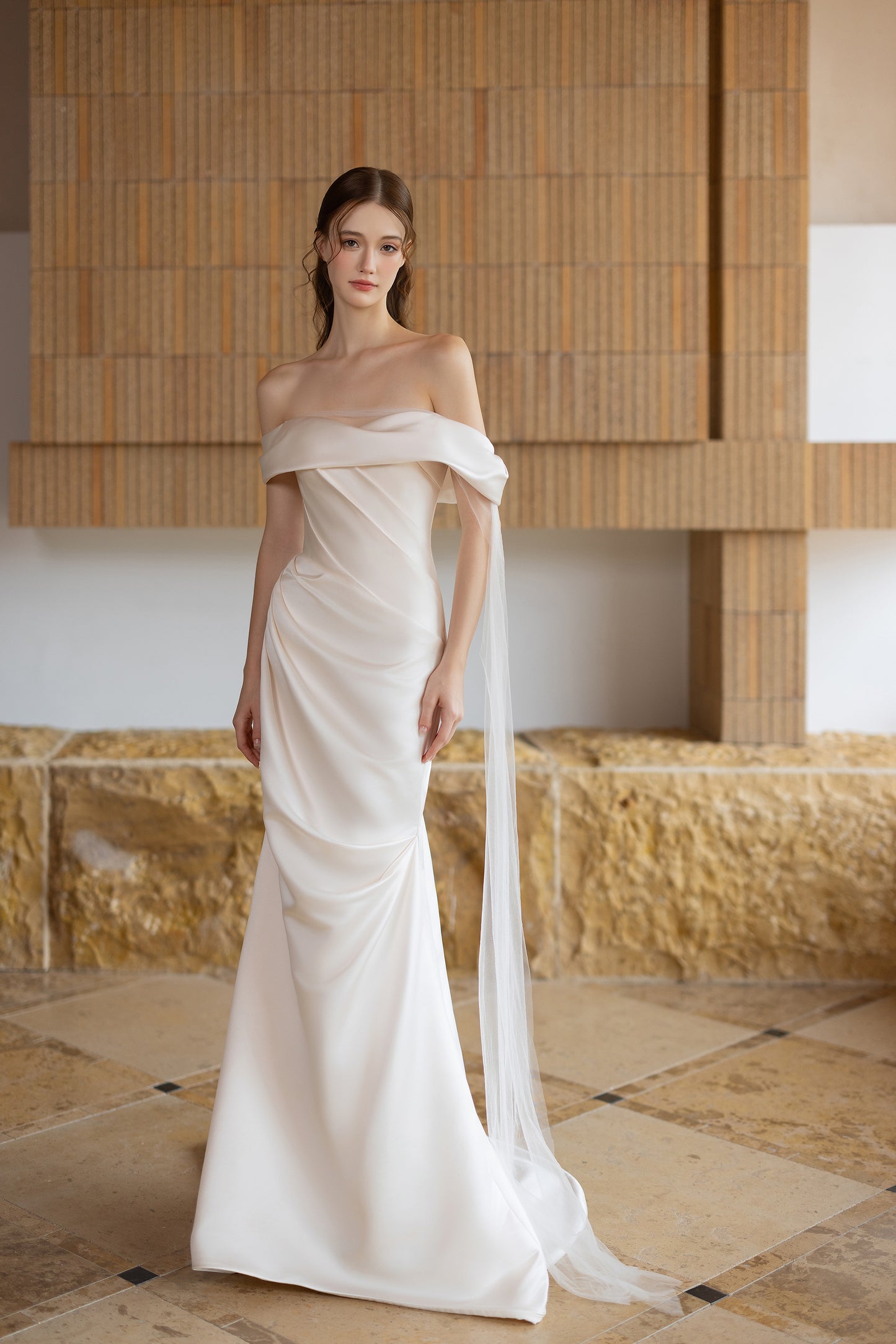 Minimalist satin off-the-shoulder sheath wedding dress with draped bodice and flowing train
